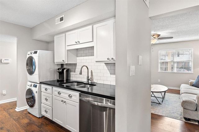 kitchen with visible vents, stacked washer and clothes dryer, dark countertops, white cabinetry, and stainless steel dishwasher