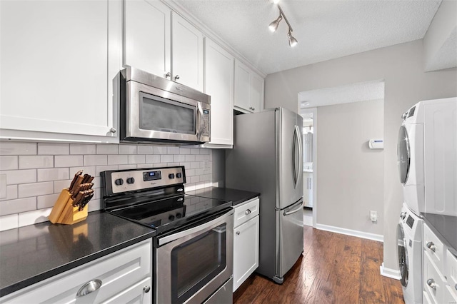 kitchen featuring dark countertops, stacked washer / drying machine, stainless steel appliances, white cabinetry, and backsplash