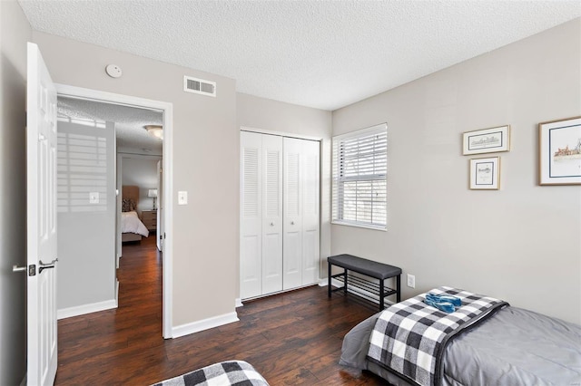 bedroom featuring dark wood-style floors, a closet, visible vents, a textured ceiling, and baseboards