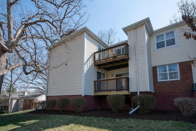 rear view of property with a balcony, brick siding, and a yard