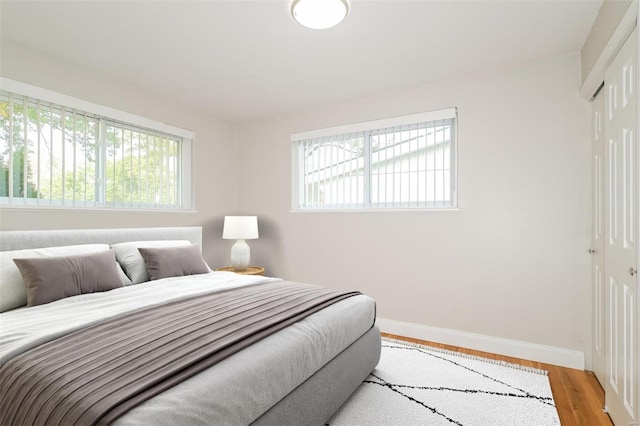 bedroom with light wood-type flooring, a closet, multiple windows, and baseboards
