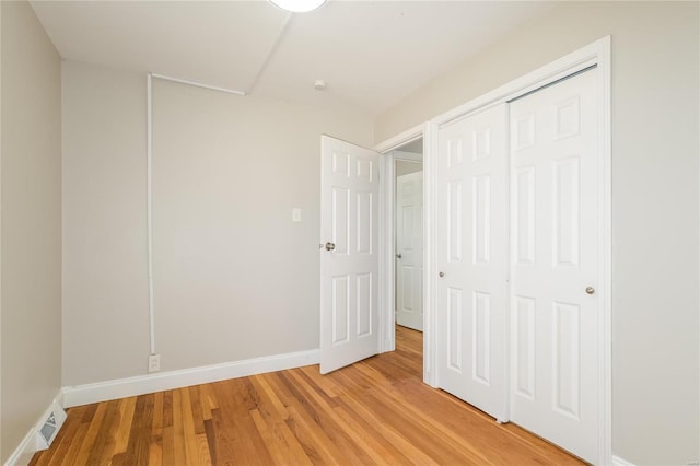 unfurnished bedroom featuring visible vents, a closet, light wood-style flooring, and baseboards