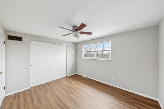 unfurnished bedroom featuring baseboards, visible vents, a closet, and wood finished floors