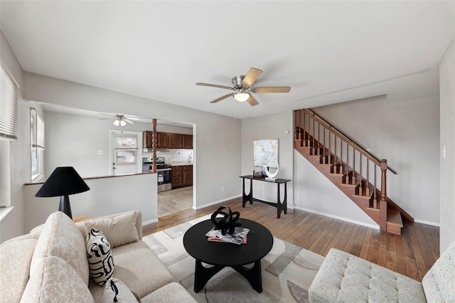 living area featuring a ceiling fan, light wood-type flooring, baseboards, and stairs