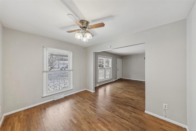 empty room with ceiling fan, wood finished floors, visible vents, and baseboards