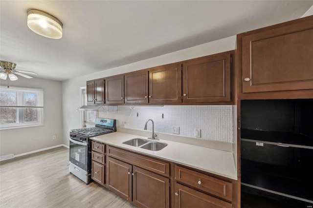 kitchen with light countertops, backsplash, light wood-style floors, a sink, and stainless steel gas range