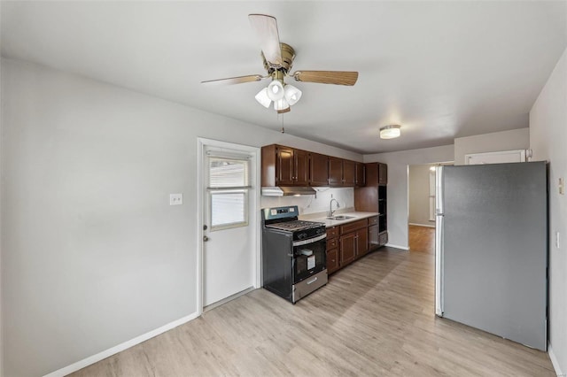 kitchen with a sink, light countertops, light wood-type flooring, freestanding refrigerator, and gas range oven