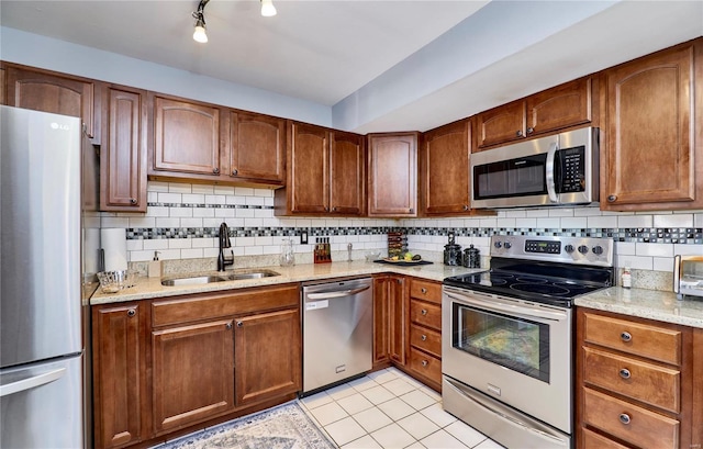 kitchen with light stone counters, tasteful backsplash, appliances with stainless steel finishes, brown cabinetry, and a sink