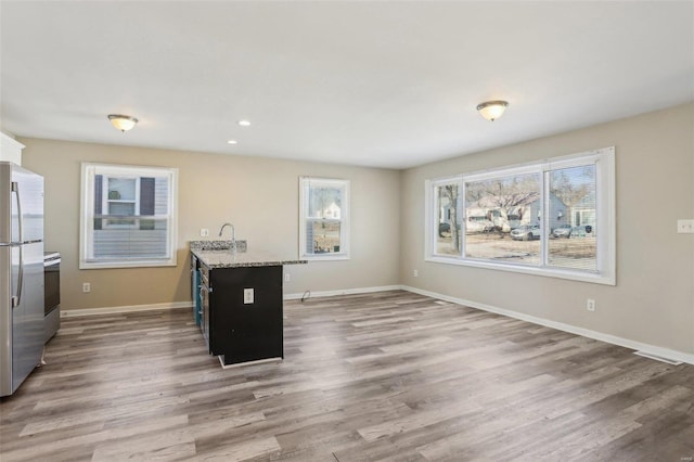 kitchen with recessed lighting, a sink, wood finished floors, baseboards, and stainless steel fridge