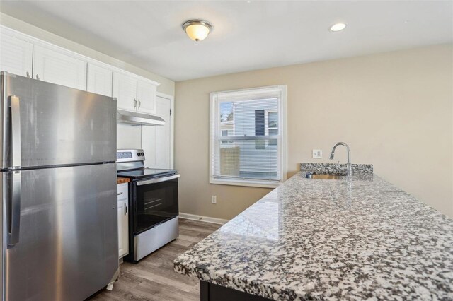 kitchen featuring appliances with stainless steel finishes, light wood-type flooring, under cabinet range hood, white cabinetry, and a sink
