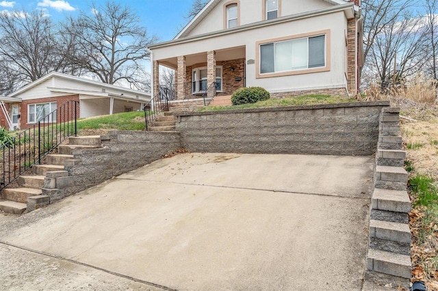 view of front facade featuring covered porch, stone siding, stairway, and stucco siding