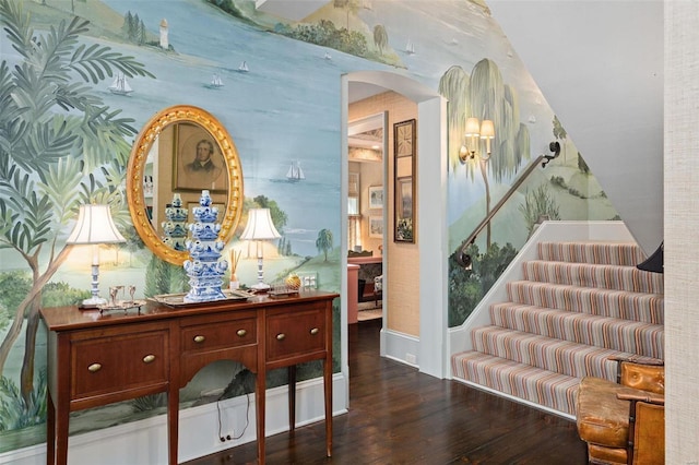 corridor featuring arched walkways, wallpapered walls, baseboards, and wood finished floors