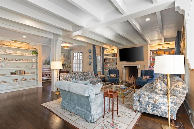 living area with beamed ceiling, built in features, a fireplace, and wood finished floors