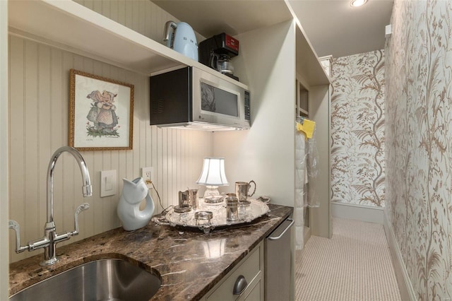 kitchen with tile patterned flooring, stainless steel microwave, dark stone countertops, and a sink