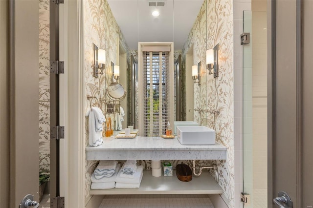 bathroom with a sink, tiled shower, and wallpapered walls