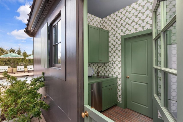 exterior space with wallpapered walls, green cabinets, brick floor, and a sink