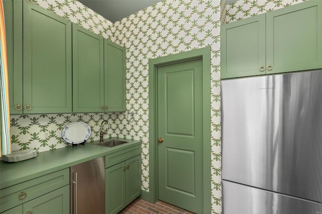 kitchen featuring a sink, wallpapered walls, freestanding refrigerator, and green cabinetry