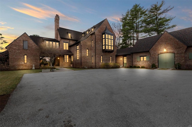 view of front of property featuring brick siding, curved driveway, and a chimney