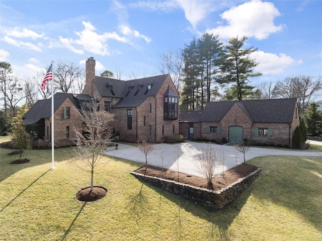 back of house featuring a yard, brick siding, concrete driveway, and a chimney