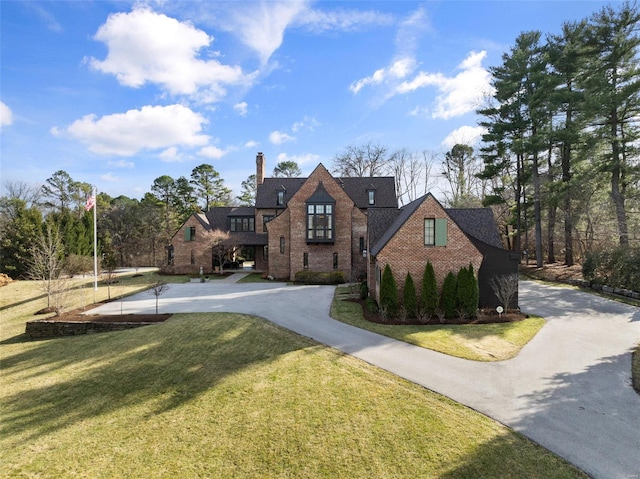 view of front of home featuring brick siding, driveway, a chimney, and a front yard