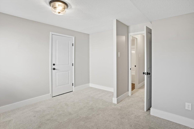 unfurnished bedroom with light colored carpet, a textured ceiling, and baseboards