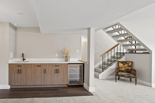 bar featuring wine cooler, stairway, a sink, a textured ceiling, and baseboards