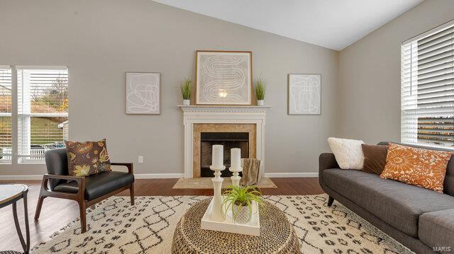 living room with a fireplace with flush hearth, a wealth of natural light, light wood-type flooring, and vaulted ceiling