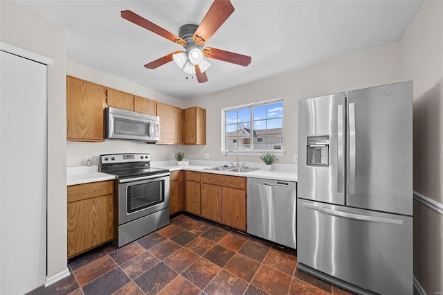 kitchen with a sink, light countertops, appliances with stainless steel finishes, stone finish flooring, and brown cabinetry