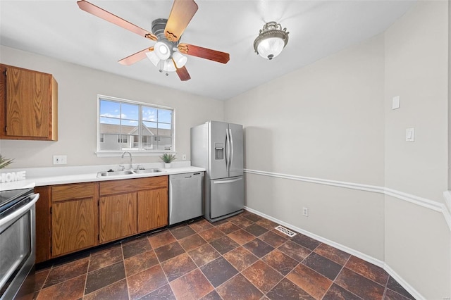 kitchen with a sink, baseboards, light countertops, appliances with stainless steel finishes, and brown cabinetry