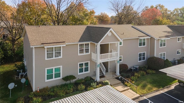 view of front of home featuring a balcony, roof with shingles, uncovered parking, a front lawn, and central AC