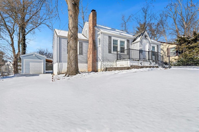 view of snowy exterior with a garage, a chimney, and an outbuilding