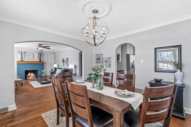 dining room with dark wood-type flooring, arched walkways, crown molding, and a fireplace