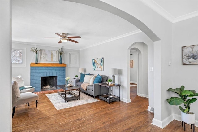 living area featuring baseboards, arched walkways, wood finished floors, crown molding, and a fireplace