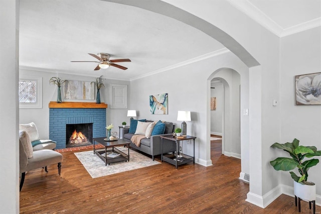 living area featuring arched walkways, baseboards, a brick fireplace, dark wood-style floors, and crown molding