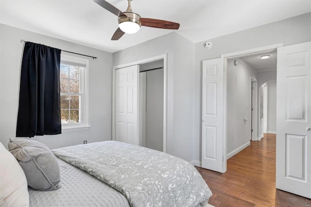 bedroom featuring baseboards, arched walkways, ceiling fan, dark wood-type flooring, and a closet