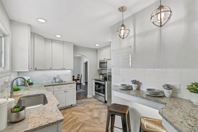 kitchen featuring arched walkways, white cabinets, hanging light fixtures, stainless steel appliances, and a sink