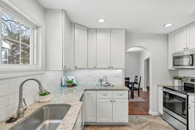 kitchen with arched walkways, white cabinets, a sink, stainless steel appliances, and backsplash