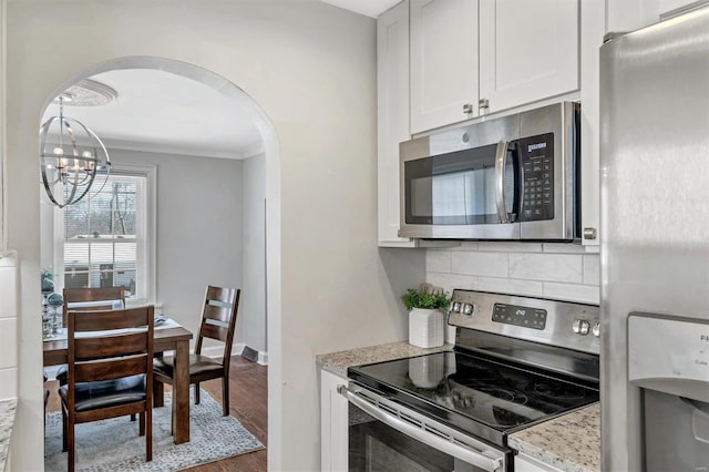 kitchen featuring arched walkways, tasteful backsplash, appliances with stainless steel finishes, white cabinetry, and light stone countertops