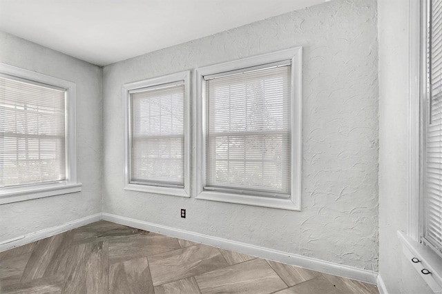 spare room featuring a textured wall and baseboards