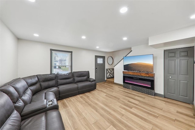 living room featuring baseboards, light wood-type flooring, a glass covered fireplace, and recessed lighting