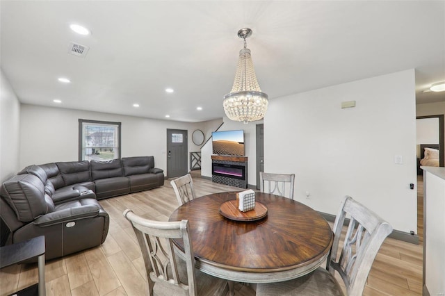 dining area featuring recessed lighting, visible vents, light wood-type flooring, a glass covered fireplace, and an inviting chandelier