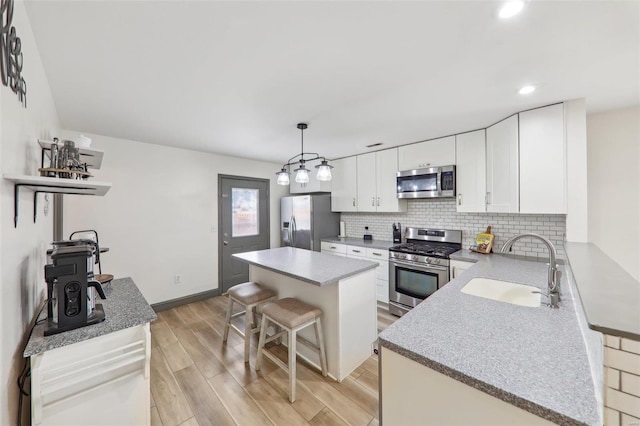 kitchen featuring light wood finished floors, tasteful backsplash, a center island, stainless steel appliances, and a sink