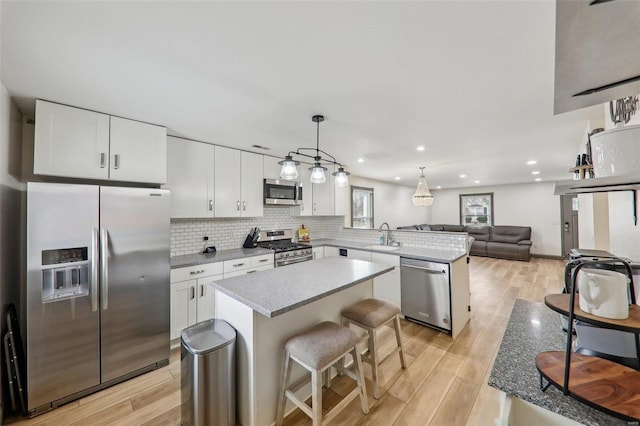 kitchen with decorative backsplash, appliances with stainless steel finishes, open floor plan, a peninsula, and light wood-style floors