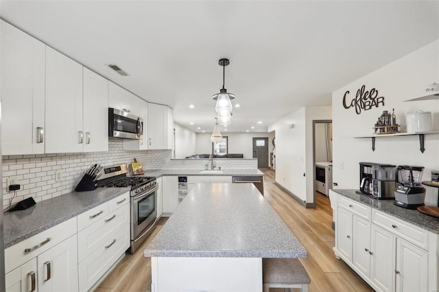 kitchen with light wood-style flooring, a kitchen island, a peninsula, stainless steel appliances, and a sink