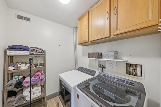 clothes washing area featuring washing machine and dryer, visible vents, cabinet space, and light wood finished floors