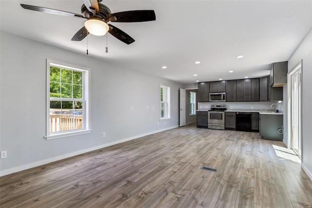 kitchen with light wood finished floors, open floor plan, stainless steel appliances, light countertops, and dark brown cabinets