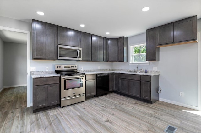 kitchen with baseboards, visible vents, stainless steel appliances, light wood-type flooring, and a sink