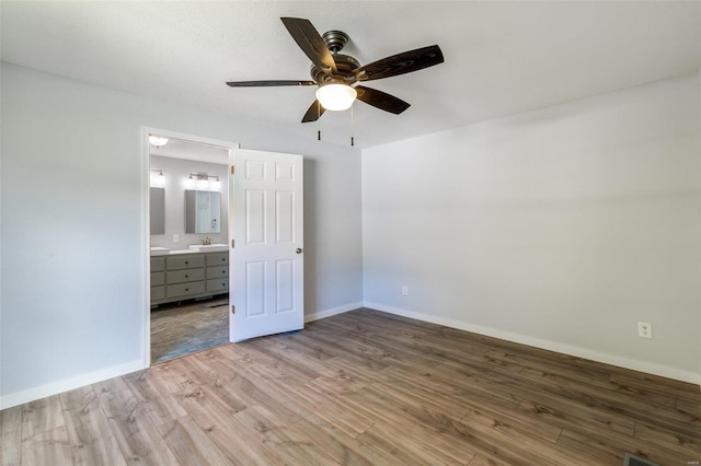 unfurnished bedroom featuring a sink, light wood-style flooring, baseboards, and ensuite bath