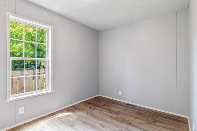 spare room featuring a textured ceiling, wood finished floors, visible vents, and a decorative wall