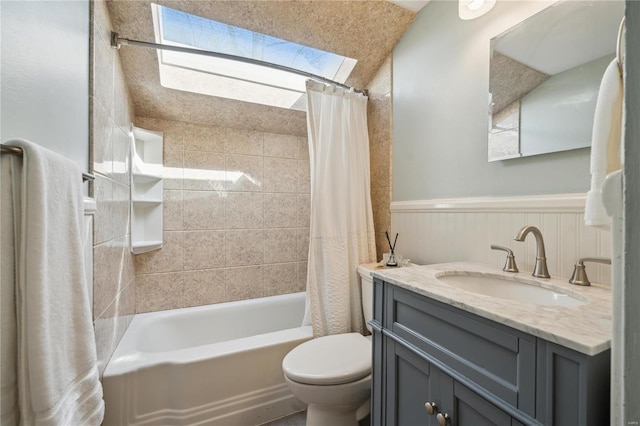 full bathroom featuring toilet, a skylight, wainscoting, shower / bath combination with curtain, and vanity